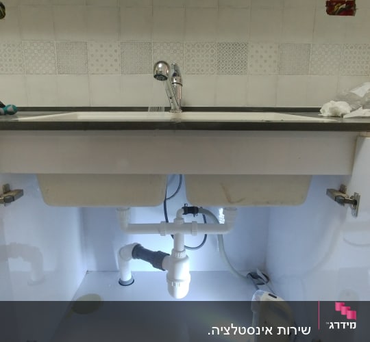 כיור מטבח עם צנרת ותאורה מתחת לארון